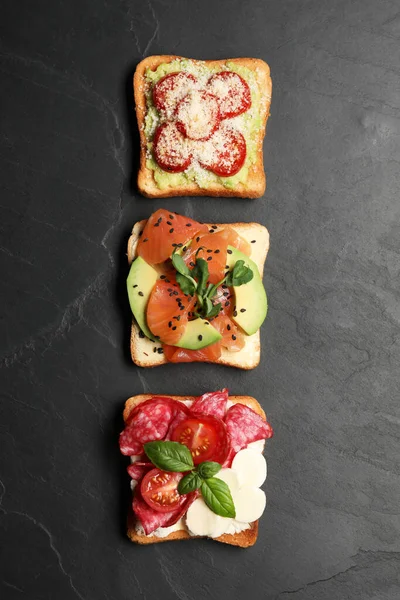 Tasty toasts with different toppings on black table, flat lay