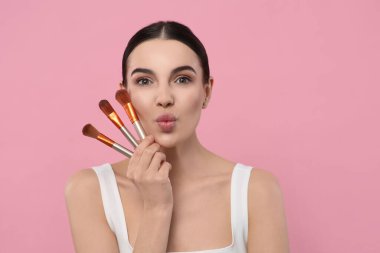 Farklı makyaj fırçaları ve pembe arka planı olan güzel bir kadın. Metin için boşluk