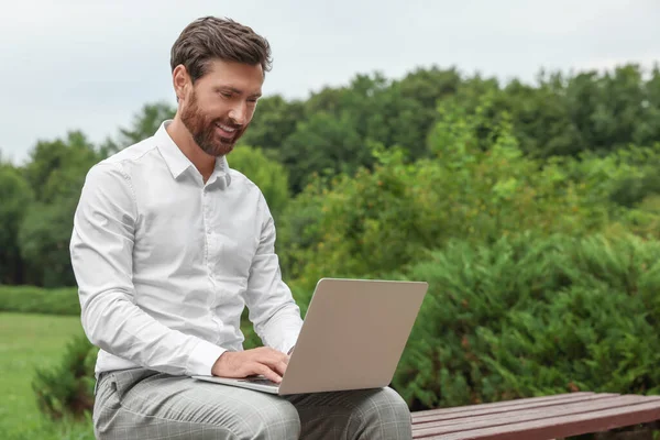 Handsome businessman with laptop on bench in park