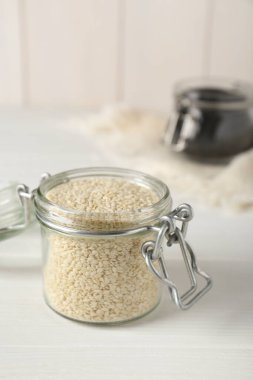 Beyaz ahşap masada susam tohumlu cam kavanozlar.