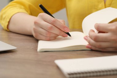 Kapalı alandaki ahşap masada deftere yazı yazan kadın.