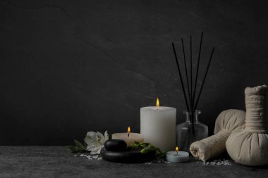 Farklı bakım ürünleriyle güzel bir spa kompozisyonu ve siyah arka planda koyu gri masada mum yakmak. Metin için boşluk