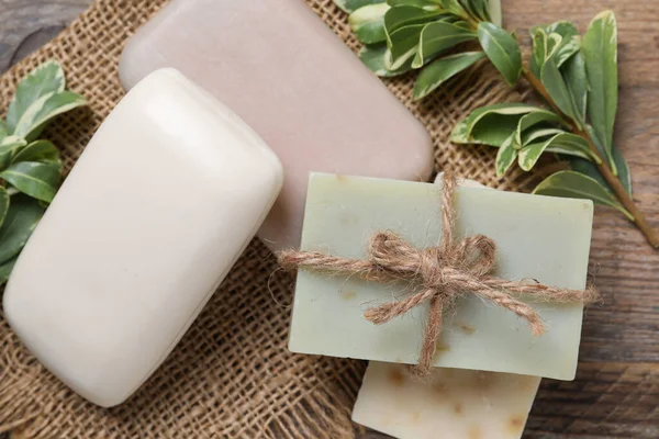 Different soap bars and green plants on wooden table, flat lay