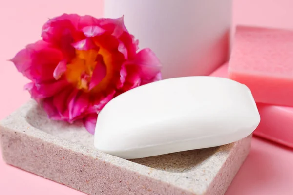 Dish with soap bar and flower on pink background, closeup