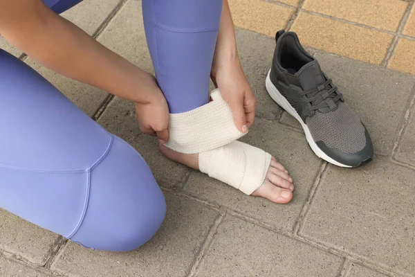 Woman wrapping foot in medical bandage outdoors, closeup