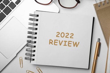 Text 2022 Review written in notebook, laptop, pen and glasses on white table, flat lay clipart