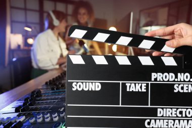 Çekim filmi. İkinci asistan kamera film setinde radyo çalışanları (aktörler) önünde el çırpma tahtası tutuyor.