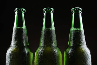 Siyah arka planda bir sürü bira şişesi, yakın plan.