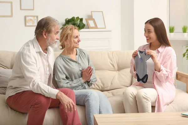 Happy woman showing her parents baby\'s bodysuit at home. Grandparents\' reaction to future grandson