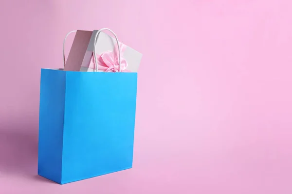 Light blue paper shopping bag with gift box on pink background. Space for text