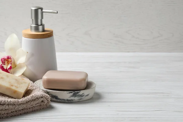 Soap bars, dispenser and terry towel on white wooden table. Space for text