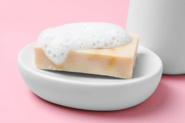 Dish with soap bar and fluffy foam on pink background, closeup