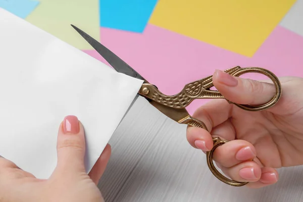 Woman cutting paper with scissors at white wooden table, closeup