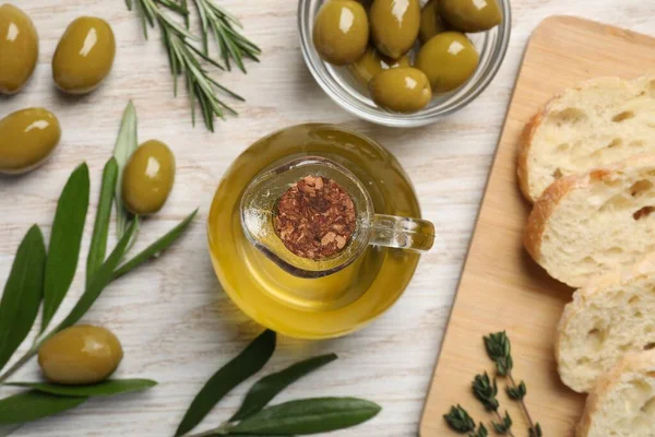 Cooking oil in jug, olives, herbs and ciabatta bread on wooden table, flat lay