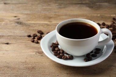 Bir fincan sıcak aromatik kahve ve ahşap masada kavrulmuş fasulye, mesaj için yer.