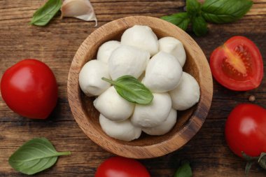Lezzetli mozzarella topları kasede, domates ve fesleğen yaprakları ahşap masada, düz yerde..