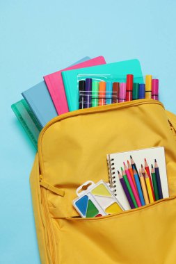 Açık mavi arkaplanda farklı okul kırtasiyesine sahip sırt çantası, üst görünüm