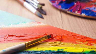 Fırçalar ve paletler ahşap masa üzerinde renkli karışık boyalar, yakın plan.