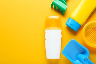 Farklı güneş ürünleri ve turuncu arka planda plastik plaj oyuncakları. Metin için boşluk