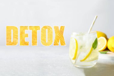 Açık gri masada bir bardak limon suyu ve kelime Detox