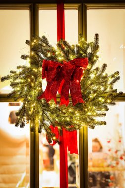 Güzel bir Noel çelengi. Kapısında kurdeleler ve şenlik ışıkları asılı.