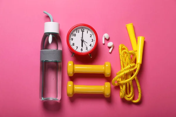 Bottle of water, alarm clock and sports equipment on pink background, flat lay. Morning exercise