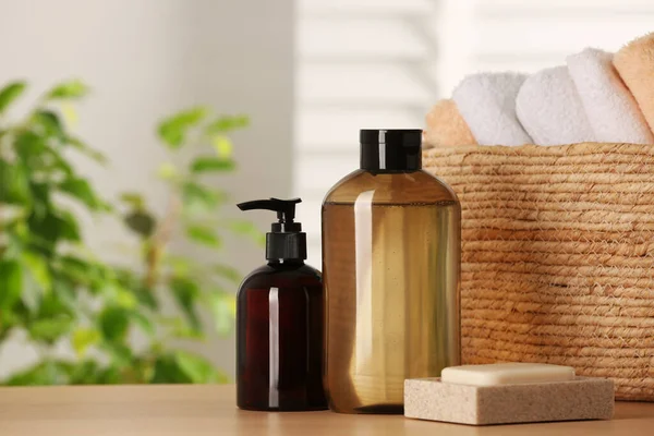 Solid shampoo bar and bottles of cosmetic product on wooden table in bathroom