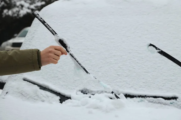 Woman cleaning car wiper blades covered with snow outdoors, closeup