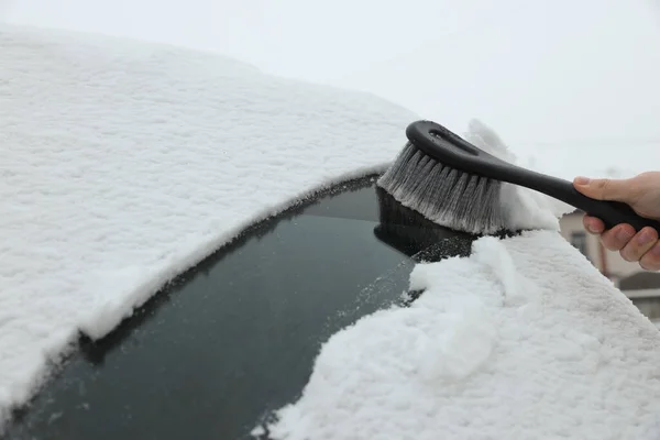 Woman cleaning car windshield from snow with brush, closeup