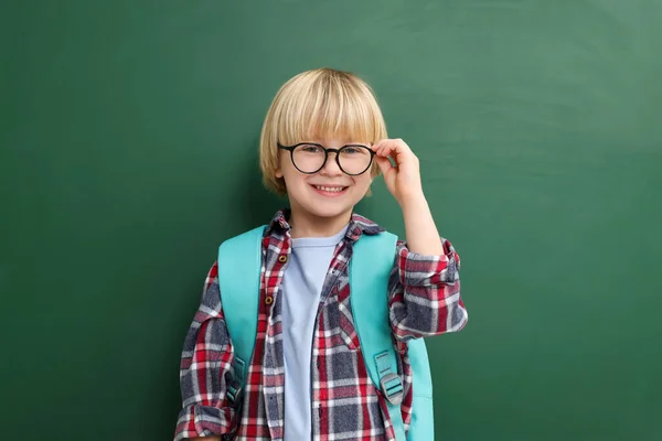 Happy little school child with backpack near chalkboard