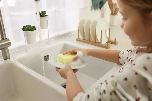 Little girl washing plate above sink indoors, closeup