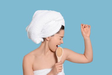 Havlu giymiş duygusal bir kadın açık mavi arka planda çalılara doğru şarkı söylüyor. Spa tedavisi