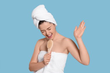 Havlu giymiş duygusal bir kadın açık mavi arka planda çalılara doğru şarkı söylüyor. Spa tedavisi