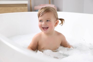 Şirin küçük kız evde köpüklü banyo yapıyor.