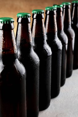 Açık kahverengi arka plana karşı gri masada bir sürü bira şişesi, yakın plan.