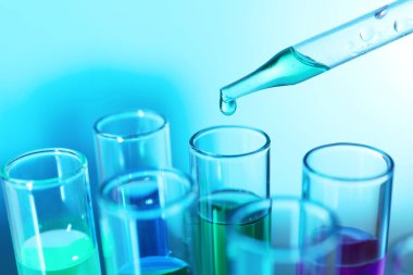 Bulanık arkaplanda pipetten test tüpüne sıvı damlatılıyor.