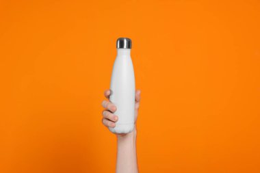 Turuncu arka planda içkili termo şişe tutan adam, yakın plan.