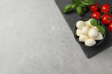 Lezzetli mozzarella topları, fesleğen ve domatesler açık gri masada, düz yerde. Metin için boşluk