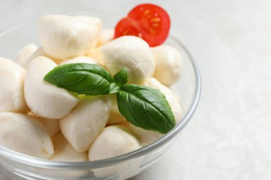 Nefis mozzarella topları ve fesleğen yaprakları açık gri masada cam kasede, yakın plan.