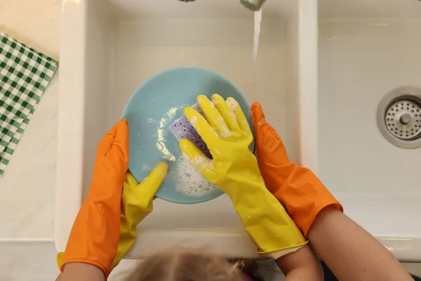 Mother and daughter in protective gloves washing plate above sink, top view