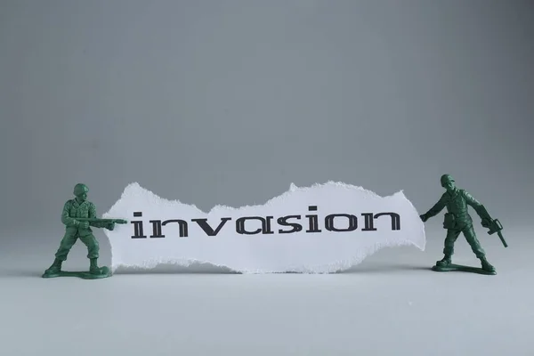Paper with word Invasion and toy soldiers on light grey background