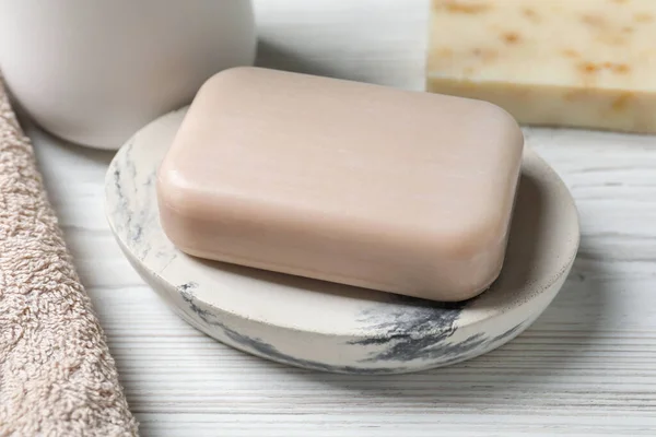 Dish with soap bar on white wooden table, closeup