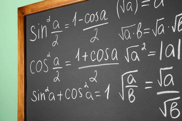 Chalkboard with many different math formulas on green wall, closeup