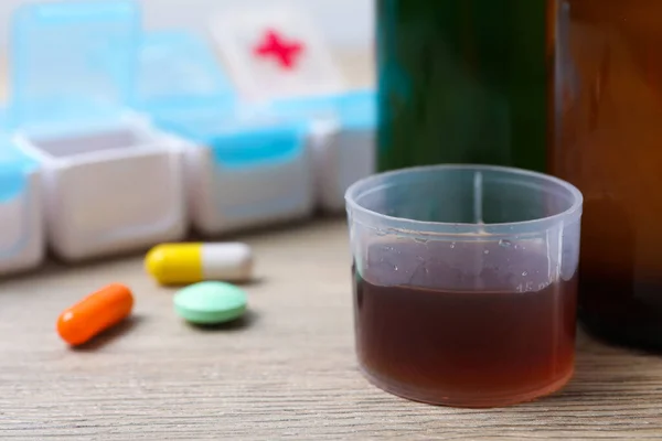 Measuring cup with syrup, pills on white table, closeup and space for text. Cold medicine