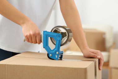 Kadın kutuya yapışkan bant yapıştırıyor. Kapalı mekanda, yakın plan.