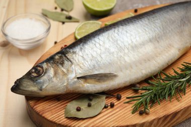 Lezzetli tuzlu ringa, körfez yaprakları, kireç, biberiye ve tuz ahşap masada, yakın plan.