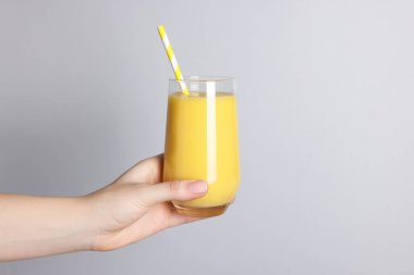 Açık gri arka planda bir bardak lezzetli smoothie tutan kadın, yakın plan.