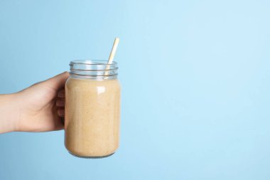 Elinde lezzetli bir meyve suyu ve açık mavi arka planda saman olan mason kavanozu tutan kadın, yakın plan. Metin için boşluk