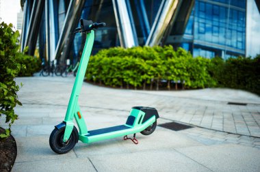 Dışarıda çalılıkların yanında yeşil elektrikli scooter var.