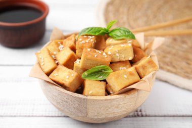 Lezzetli kızarmış tofu, fesleğen ve susam tohumlarıyla dolu bir kase beyaz ahşap masa.